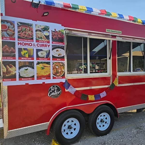 A red MOMO Curry food truck with a menu board and colorful prayer flags.
