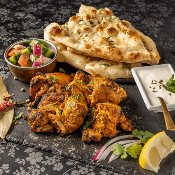 MOMO Curry's chicken tikka, naan, cucumber salad, and raita on a black slate.