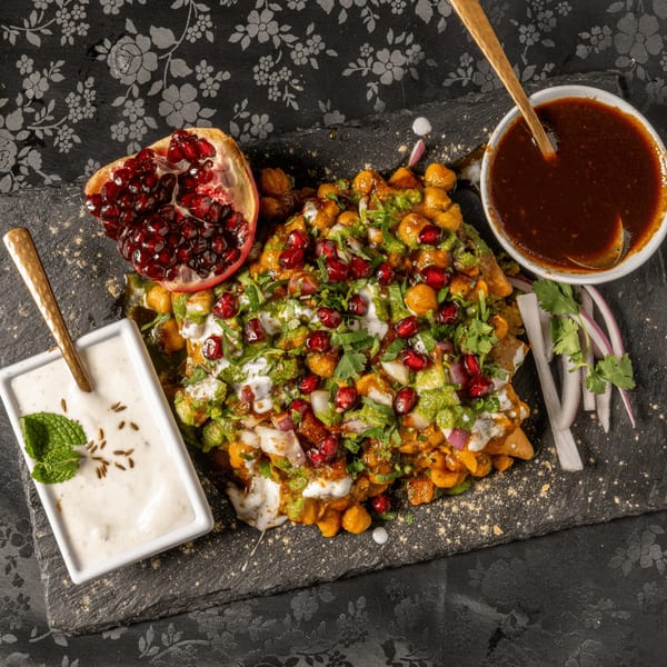 MOMO Curry's Indian chaat with chickpeas, pomegranate, sauces, and fresh herbs on a dark platter.