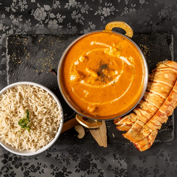 MOMO Curry's lobster curry with rice, spices, and a lobster tail on a black slate.