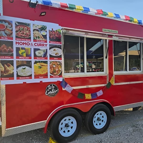 A red MOMO Curry food truck with a large menu display and colorful prayer flags.