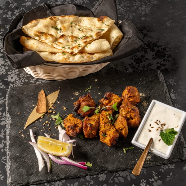 MOMO Curry's chicken tikka with naan bread, raita, lemon, and spices on a black slate.