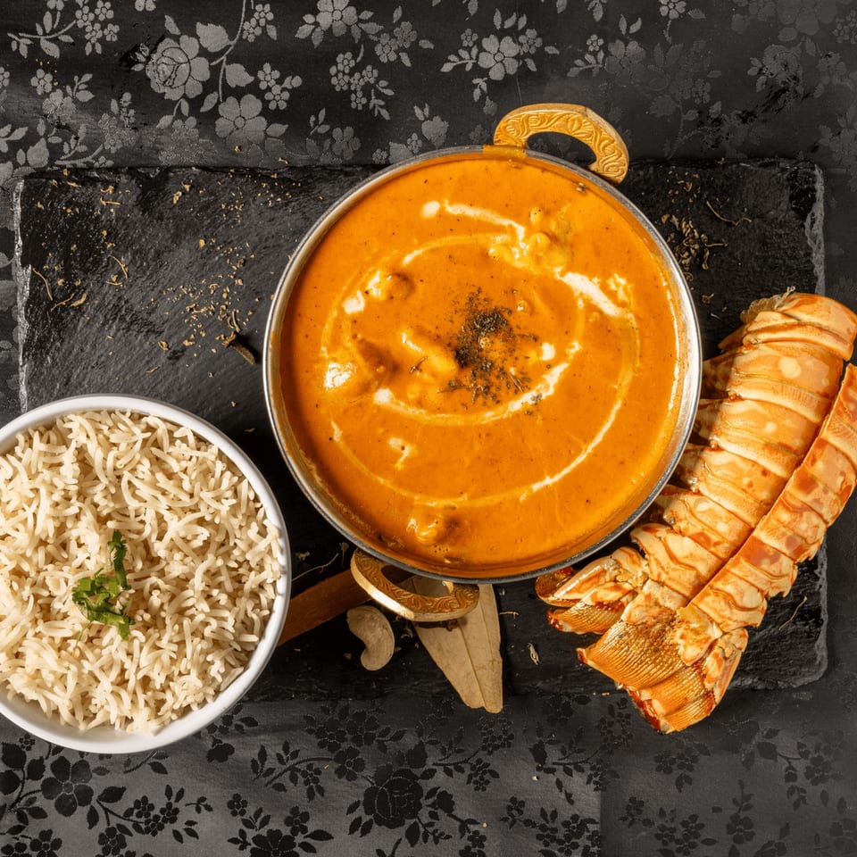 MOMO Curry's lobster curry with rice and lobster tails on a black slate.