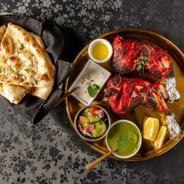 MOMO Curry's Tandoori Chicken with naan, raita, cucumber salad, mint chutney, and lemon wedges.