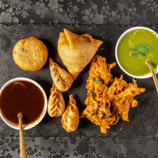 Assortment of Indian appetizers including samosas, pakoras, momos, and kachori with green and red sauces.