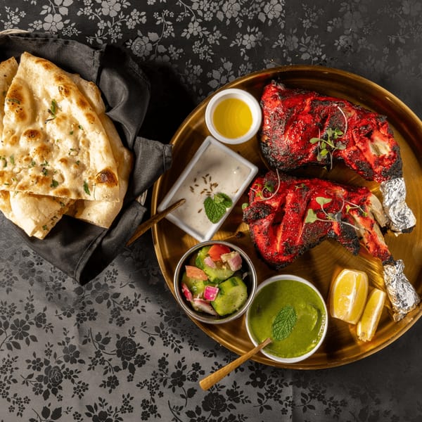 MOMO Curry's Tandoori chicken with naan, sauces, lemon, and cucumber salad on a gold tray.