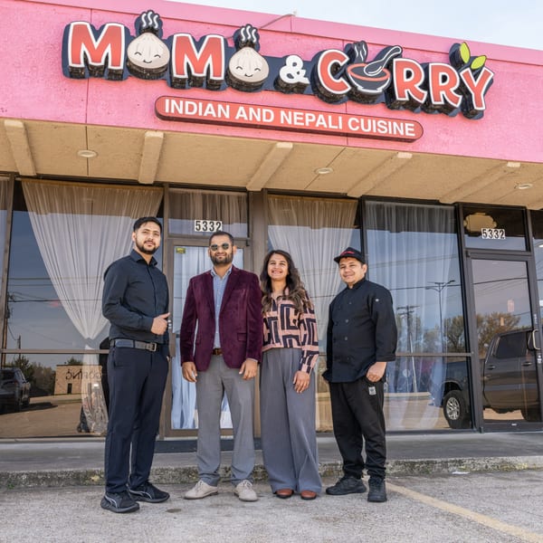 Four MOMO Curry staff members, including a chef, stand proudly in front of the restaurant's pink exterior.