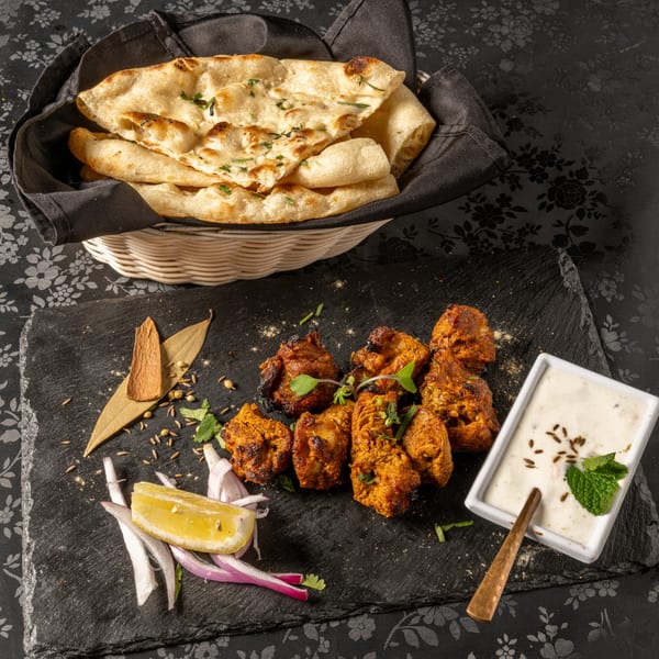 MOMO Curry's chicken tikka with naan, raita, lemon, and spices on a black slate.