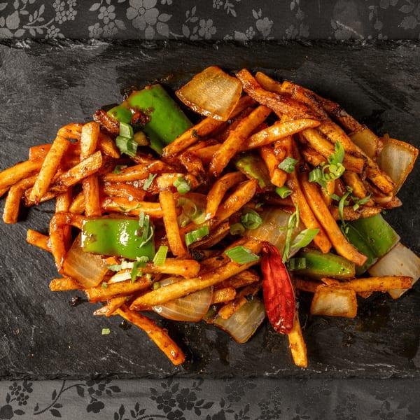 Chili garlic fries, green peppers, onions, and red chili on a dark slate board.