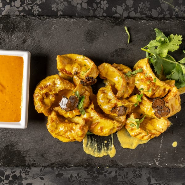 MOMO Curry's Indian momos with yellow curry sauce, truffle slices, and cilantro on a slate.
