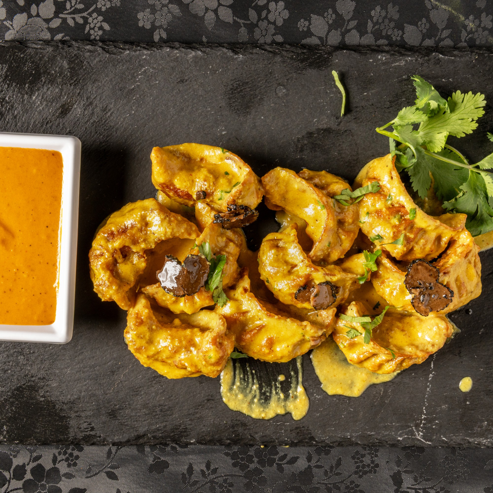 MOMO Curry's Indian momos with yellow curry sauce, truffle slices, and cilantro on a slate.